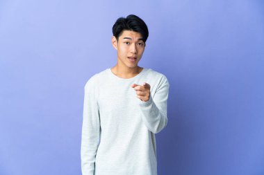 Mor arka planda izole edilmiş genç bir Çinli şaşırmış ve ön tarafı işaret ediyor.