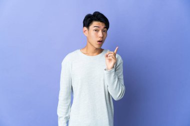 Mor arka planda izole edilmiş genç bir Çinli parmak kaldırırken çözümü bulmayı amaçlıyor.