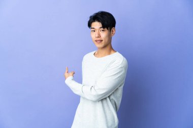 Young Chinese man isolated on purple background pointing back