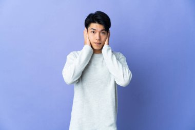 Mor arka planda izole edilmiş genç bir Çinli hayal kırıklığına uğramış ve kulaklarını kapatmış.