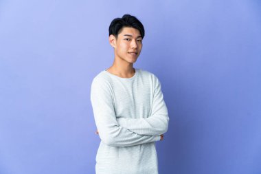 Young Chinese man isolated on purple background with arms crossed and looking forward