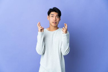 Mor arka planda izole edilmiş genç Çinli bir adam parmaklarını çapraz yapıp en iyisini diliyor.