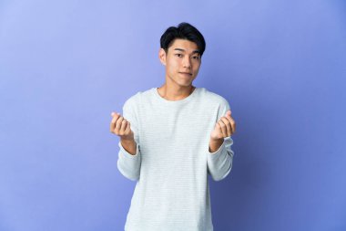 Young Chinese man isolated on purple background making money gesture but is ruined