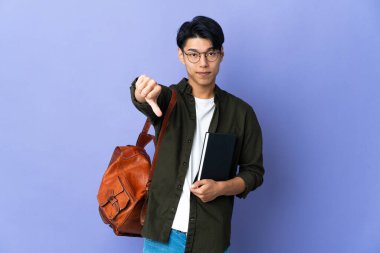 Mor arka planda izole edilmiş genç bir bayan, olumsuz ifade ile baş parmağını gösteriyor.