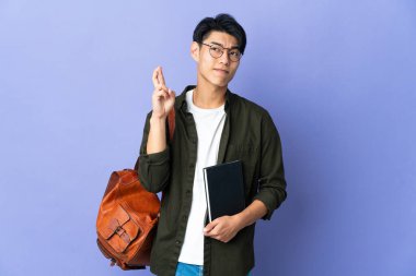 Mor arka planda izole edilmiş genç bir öğrenci kadın parmaklarını çapraz yapıp en iyisini diliyor.