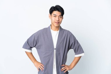 Beyaz arka planda izole edilmiş genç bir Çinli kolları kalçasında ve gülümsüyor.