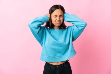 Pembe arka planda izole edilmiş genç Latin kadın hayal kırıklığına uğramış ve kulaklarını kapatmış.