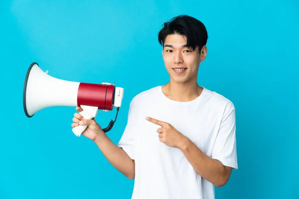 Young Chinese Man Isolated Blue Background Holding Megaphone Pointing Side — стокове фото