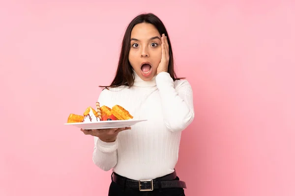 Young Brunette Woman Holding Waffles Isolated Pink Background Surprise Shocked — Stockfoto