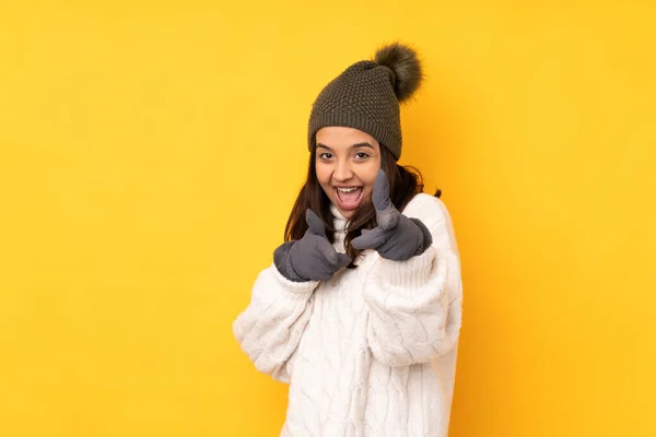 年轻女子头戴冬帽 背对孤立的黄色背景 指着前面笑着 — 图库照片