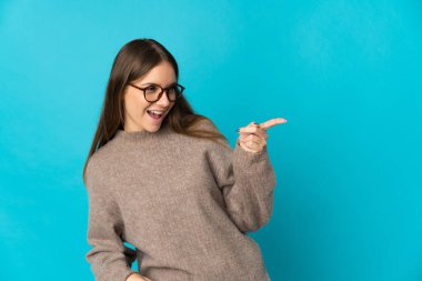 Genç Litvanyalı bir kadın mavi arka planda izole edilmiş bir şekilde parmak ucunda bir ürün sunuyor.