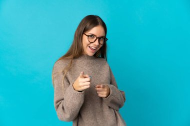 Genç Litvanyalı kadın mavi arka planda izole edilmiş, şaşırmış ve ön tarafı işaret ediyor.