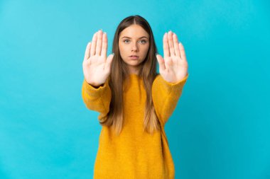 Genç Litvanyalı bir kadın mavi arka planda izole edilmiş. Durma hareketi yapıyor ve hayal kırıklığına uğruyor.