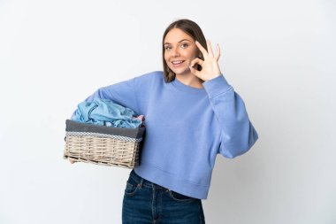 Litvanyalı genç bir kadın beyaz arka planda izole edilmiş çamaşır sepetini tutarken parmaklarıyla işaret veriyor.