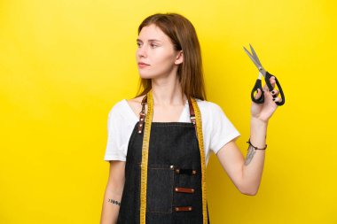 Sarı arka planda izole edilmiş genç terzi kadın yan tarafa bakıyor.