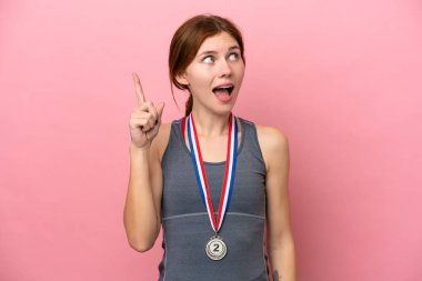 Pembe arka planda madalyaları olan genç İngiliz kadın çözümü bulmak için parmağını kaldırıyor.