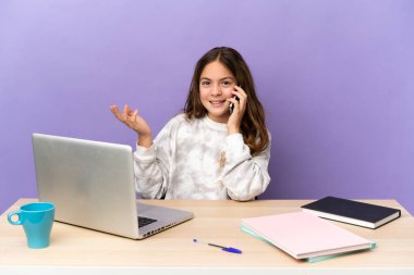 Mor arka planda dizüstü bilgisayarı olan küçük bir öğrenci kız cep telefonuyla sohbet ediyor.