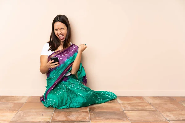 Genç Hintli Kadın Yerde Oturuyor Telefonu Zafer Pozisyonunda — Stok fotoğraf