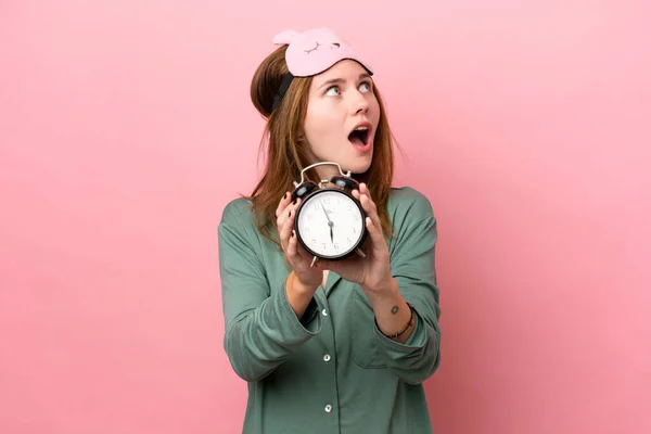 Young English Woman Pajamas Isolated Pink Background Pajamas Holding Clock — стоковое фото