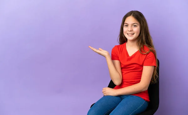 紫色の背景に隔離された椅子に座っている小さな白人の女の子は 広告を挿入するためにヤシの上に想像上のコピースペースを保持 — ストック写真