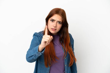 Beyaz arka planda izole edilmiş genç kızıl saçlı kadın hayal kırıklığına uğramış ve ön tarafı işaret ediyor.