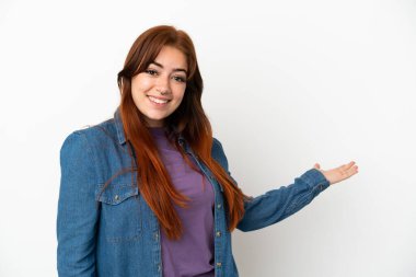 Genç kızıl saçlı kadın, beyaz arka planda izole edilmiş. Davet etmek için ellerini yana uzatıyor.