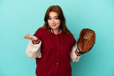 Beyzbol oynayan genç kızıl saçlı kadın, mavi arka planda izole edilmiş, kuşkuları olan ve ellerini kaldıran.