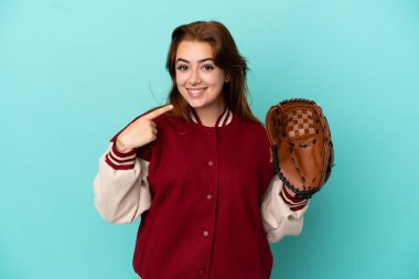 Beyzbol oynayan genç kızıl saçlı kadın mavi arka planda izole edilmiş bir şekilde baş parmak hareketi yapıyor.