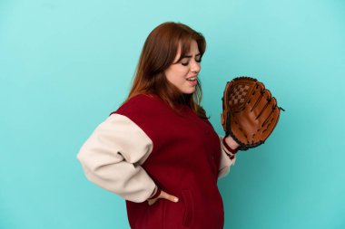 Beyzbol oynayan genç kızıl saçlı kadın, mavi arka planda izole edilmiş, gayret gösterdiği için sırt ağrısından muzdarip.