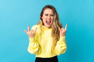 Mavi arka planda izole edilmiş genç Brezilyalı kadın boynuz hareketi yapıyor.