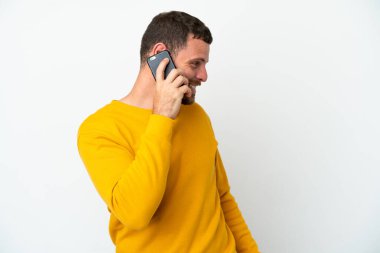 Beyaz arka planda izole edilmiş genç Brezilyalı bir adam cep telefonuyla sohbet ediyor.