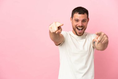 Pembe arka planda izole edilmiş genç Brezilyalı adam şaşırmış ve ön tarafı işaret ediyor.