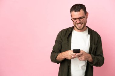 Pembe arka planda izole edilmiş genç Brezilyalı adam cep telefonuyla bir mesaj gönderiyor.