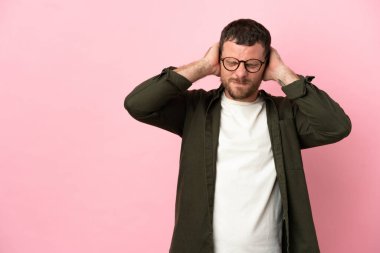 Pembe arka planda izole edilmiş genç Brezilyalı adam hayal kırıklığına uğramış ve kulaklarını kapatmış.