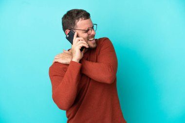 Cep telefonu kullanan genç Brezilyalı adam mavi arka planda izole edilmiş, omuz ağrısından muzdarip, çabaladığı için.