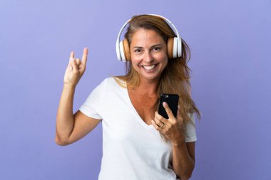 Mor arka planda izole edilmiş orta yaşlı Brezilyalı bir kadın gezici bir rock hareketi yaparak müzik dinliyor.