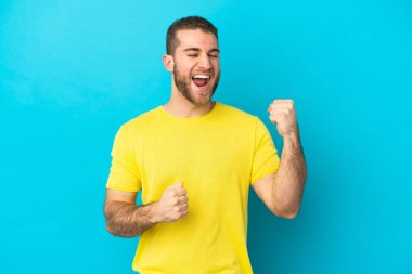 Mavi arka planda izole edilmiş yakışıklı beyaz adam zaferi kutluyor.