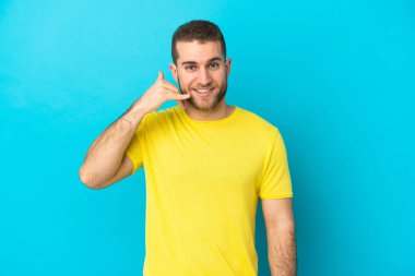 Mavi arka planda izole edilmiş yakışıklı beyaz bir adam telefon jesti yapıyor. Bana geri dönüş işareti ver.