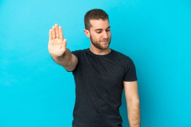 Mavi arka planda izole edilmiş yakışıklı beyaz adam dur hareketi yapıyor ve hayal kırıklığına uğruyor.