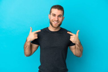 Genç, beyaz, mavi arka planda izole edilmiş genç bir adam baş parmak işareti yapıyor.