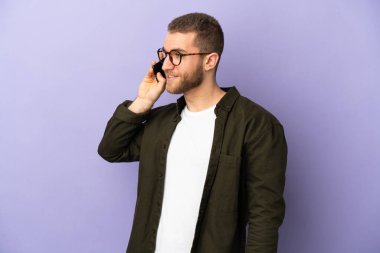 Mor arka planda izole edilmiş yakışıklı beyaz bir adam cep telefonuyla sohbet ediyor.