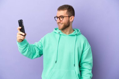 Mor arka planda izole edilmiş yakışıklı beyaz bir adam selfie çekiyor.