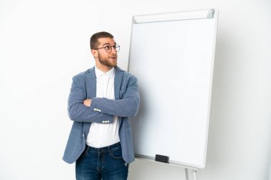 Beyaz arka planda izole edilmiş yakışıklı beyaz bir adam beyaz tahtada sunum yapıyor ve şüpheli hareketler yapıyor.