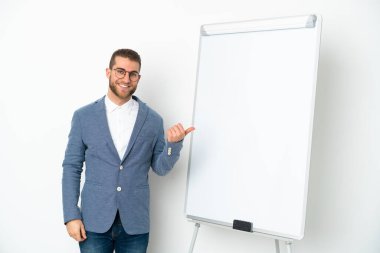 Beyaz arka planda izole edilmiş beyaz panoda sunum yapan genç bir iş kadını bir ürünü sunmak için kenarı işaret ediyor.