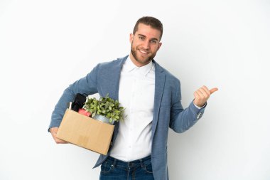 Beyaz arka planda izole edilmiş eşyalarla dolu bir kutuyu kaldırırken harekete geçen beyaz tenli genç, bir ürünü sunmak için kenarı işaret ediyor.