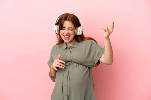 Joven Pelirroja Caucásica Aislada Sobre Fondo Rosa Embarazada Escuchando Música —  Fotos de Stock