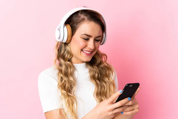 Młoda Brazylijka Odizolowana Różowym Tle Słuchając Muzyki Patrząc Telefon — Zdjęcie stockowe
