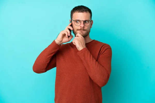 Mladý Brazilec Pomocí Mobilního Telefonu Izolované Modrém Pozadí Pochybnostmi Myšlení — Stock fotografie