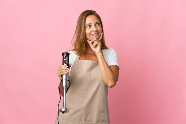 Middle Age Woman Using Hand Blender Isolated Pink Background Thinking — стоковое фото