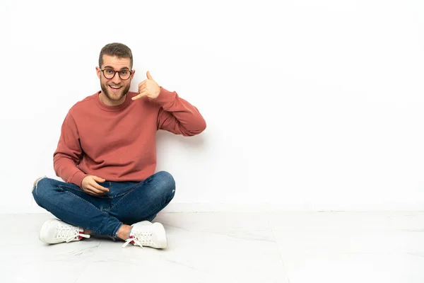 Young Handsome Man Sitting Floor Making Phone Gesture Call Back — стоковое фото